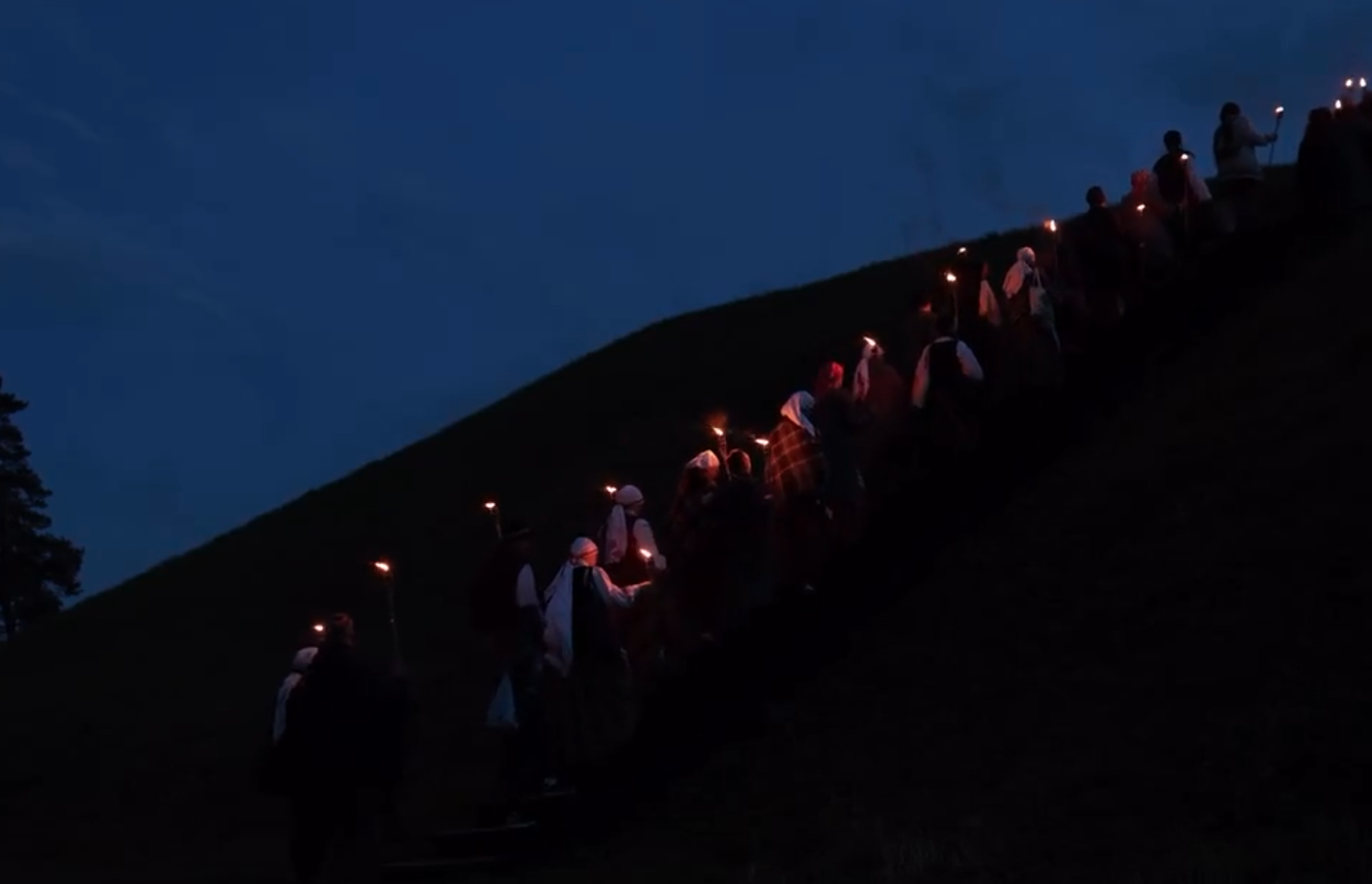People walking with torches towards top of the hill in the middle of night